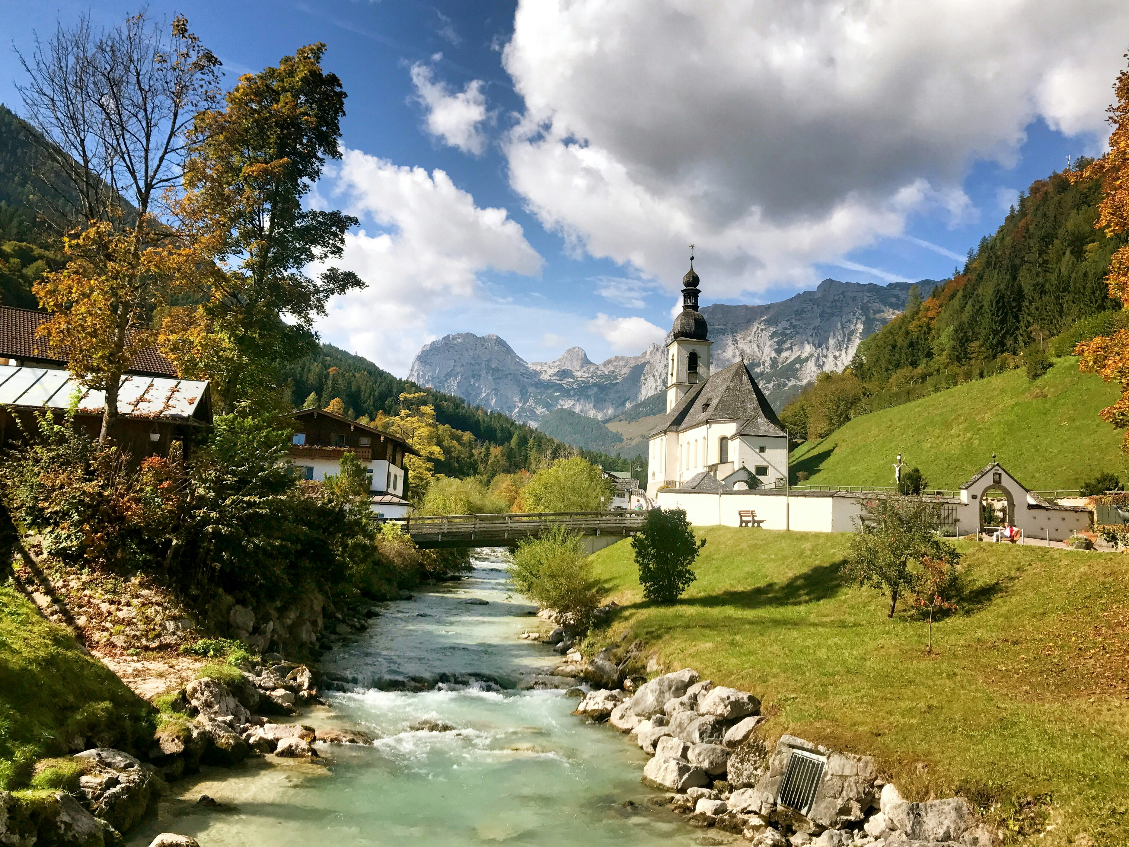 white and black concrete building near green trees and mountain under white clouds and blue sky