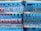 Shelves in a store are stocked with multiple brands of bottled water, neatly arranged with clear plastic bottles and colorful labels. Price tags are visible on the shelves.
