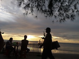 A person carrying a delivery box along a sandy beach at sunset.