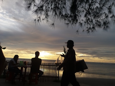 A person carrying a delivery box along a sandy beach at sunset.
