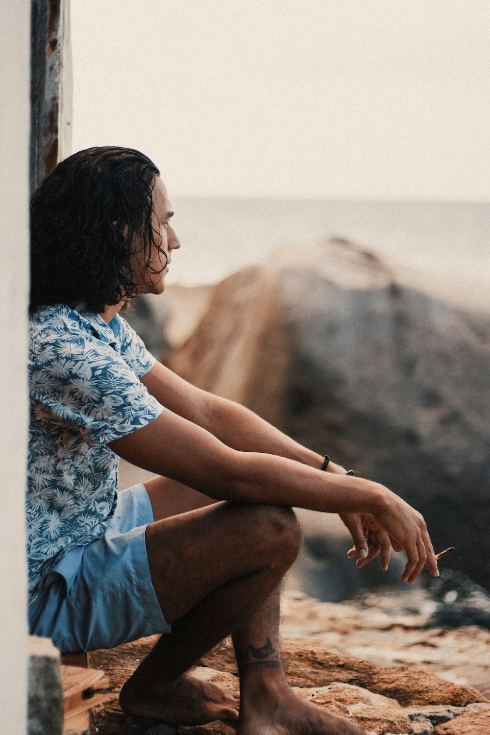 woman in blue and white floral shirt sitting on brown sand during daytime