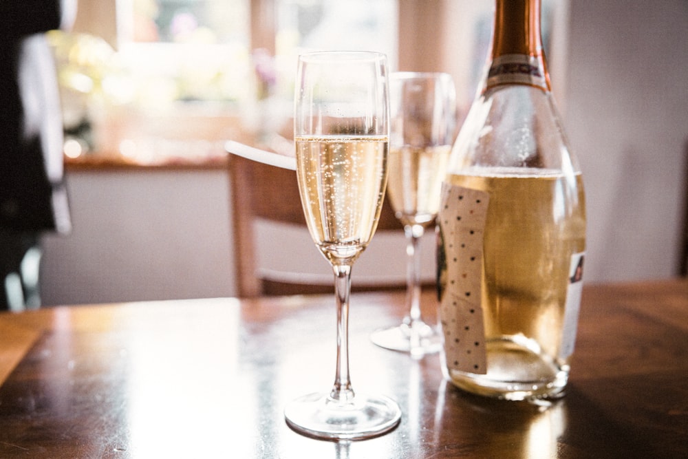 clear wine glass beside clear glass bottle on brown wooden table