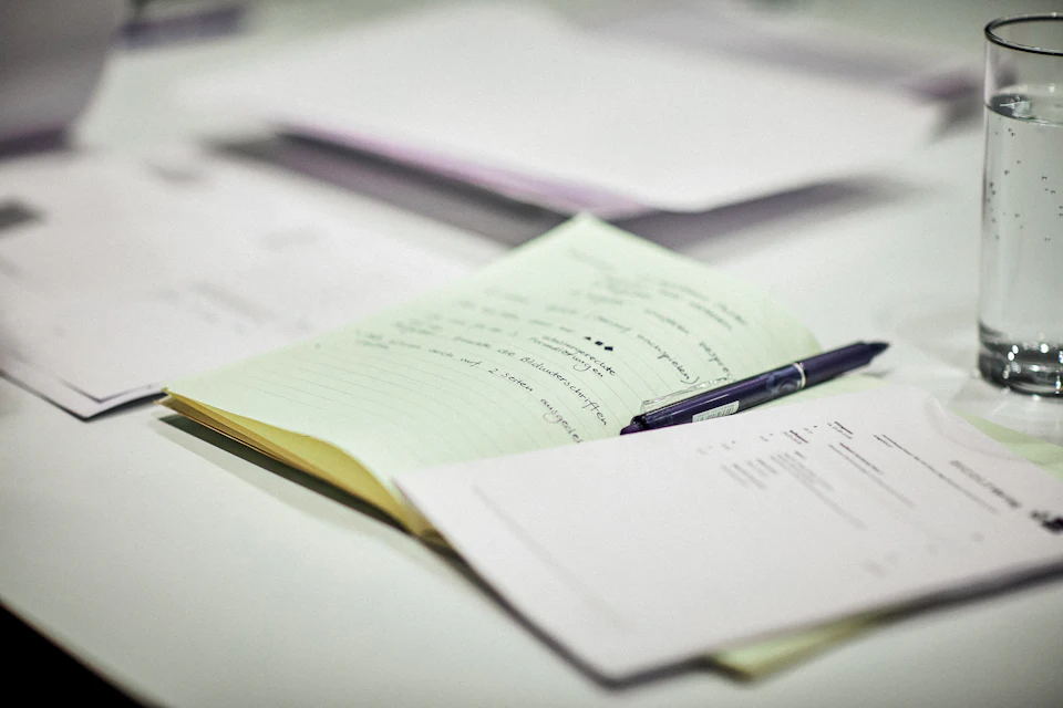 A pen resting on handwritten notes beside a glass of water
