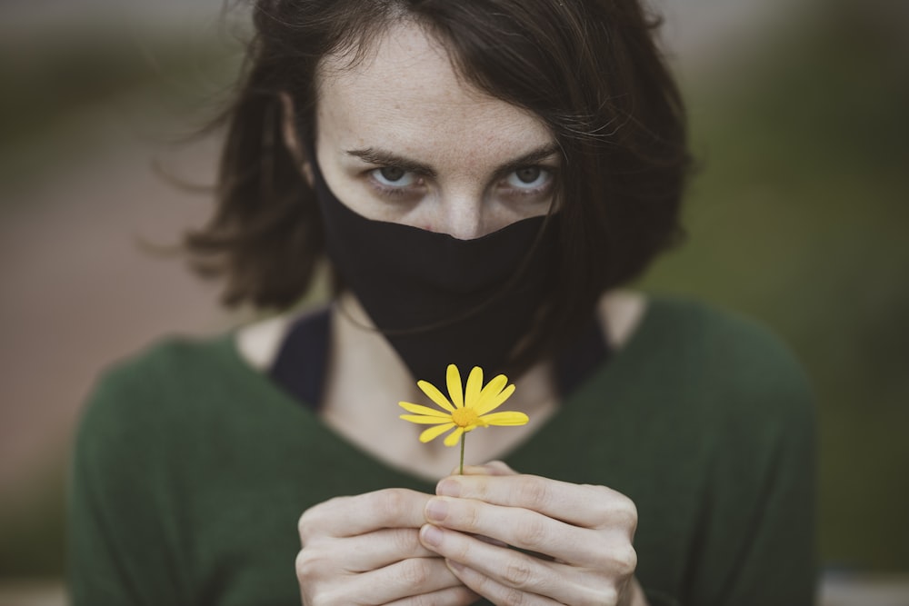 woman in green shirt holding yellow flower