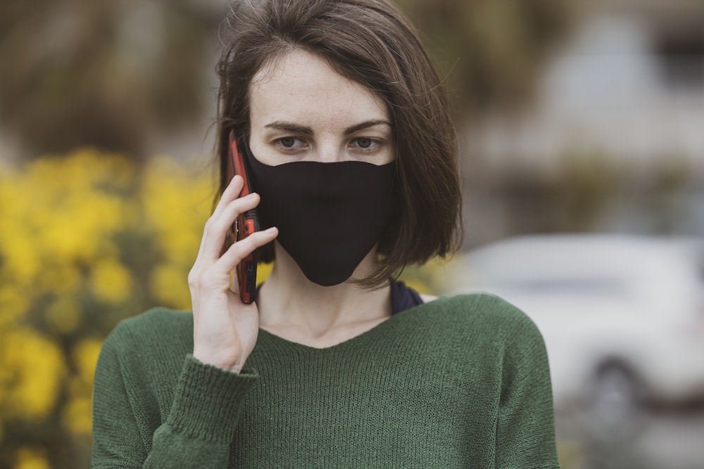 woman in green sweater holding black mask