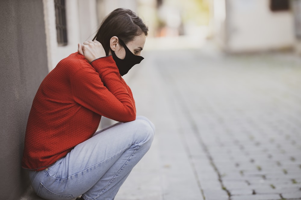 Mujer en suéter rojo y jeans de mezclilla azul sentada en pavimento de concreto