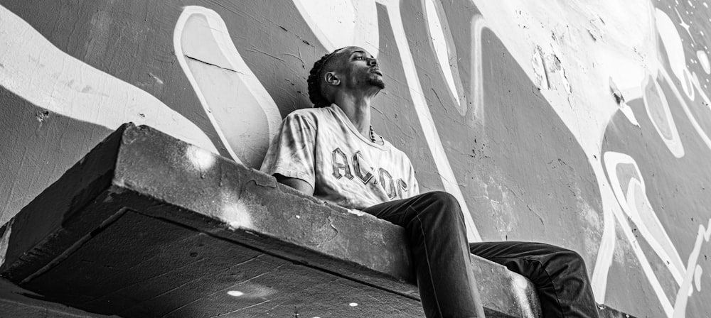 Homme en t-shirt blanc à col rond et pantalon noir assis sur un banc en béton