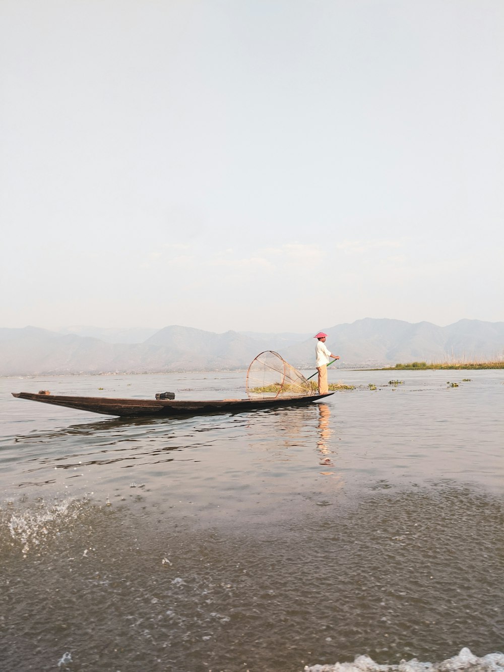 person in red shirt standing on brown wooden boat on body of water during daytime