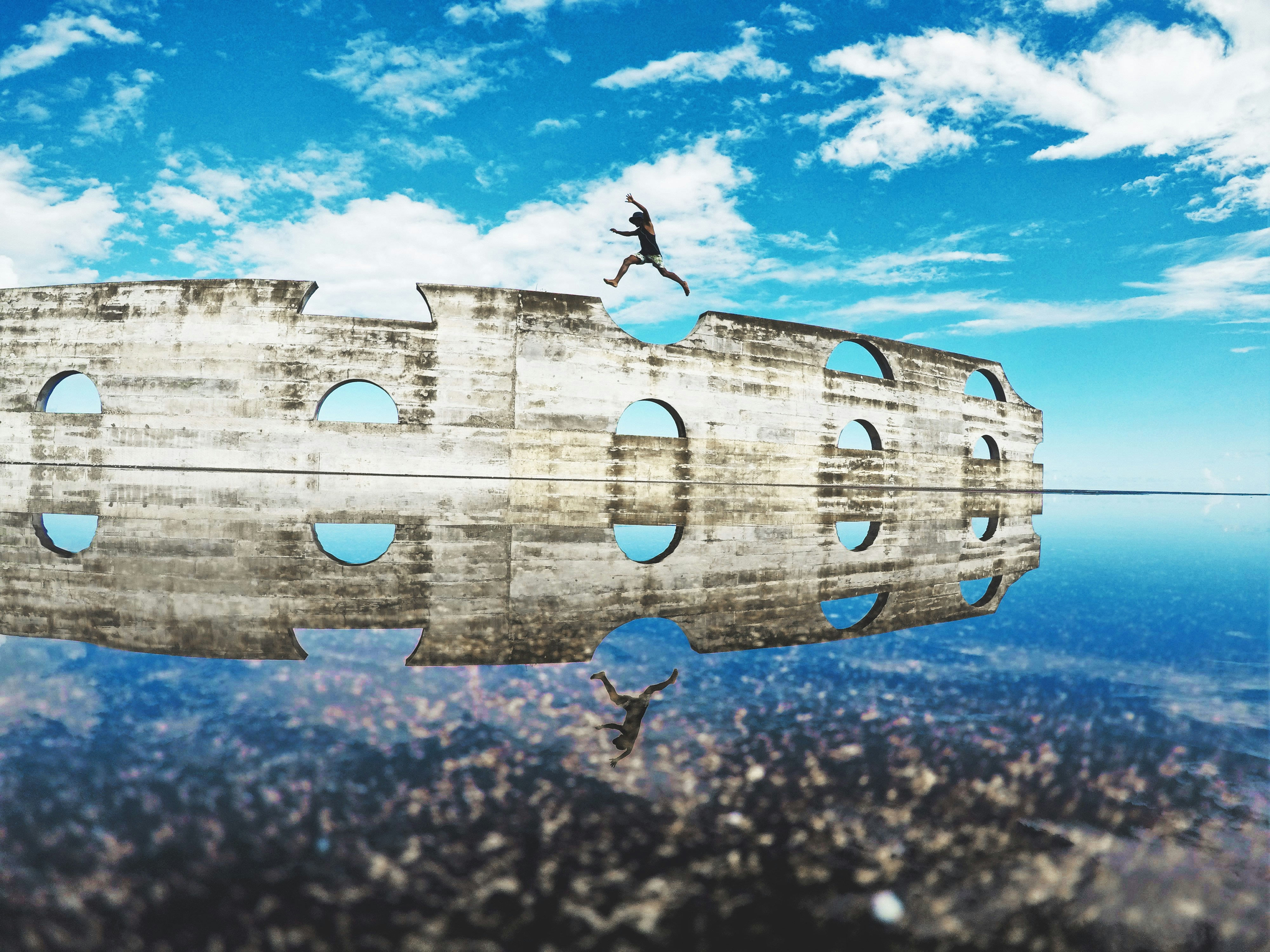 man in black shirt and black shorts jumping on brown wooden fence under blue sky during
