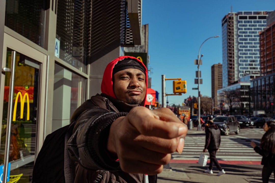 man in black jacket and red knit cap standing on sidewalk during daytime