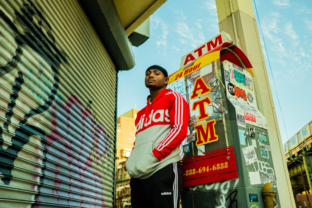 man in white and red crew neck shirt standing beside brown building during daytime