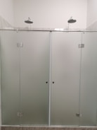 A modern shower setup with frosted glass doors and two overhead showerheads. The setting is minimalistic with clean, straight lines and a focus on functionality.