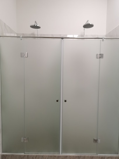 A modern shower setup with frosted glass doors and two overhead showerheads. The setting is minimalistic with clean, straight lines and a focus on functionality.