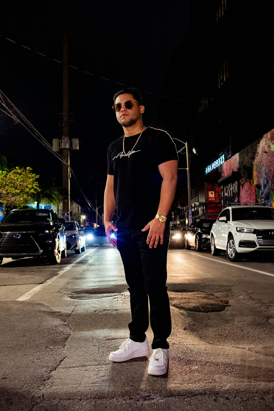 man in black crew neck t-shirt and black pants standing on sidewalk during night time