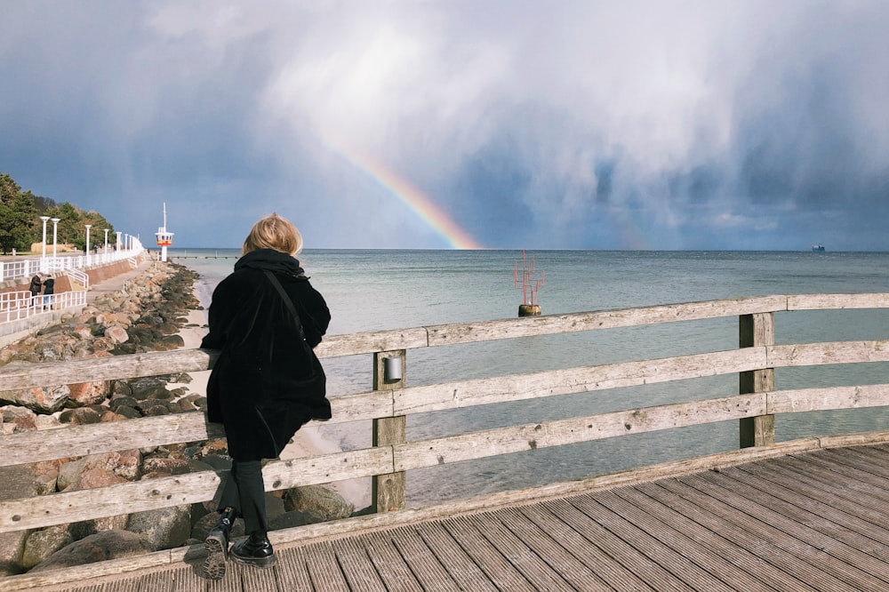 woman in black coat standing on wooden dock during daytime