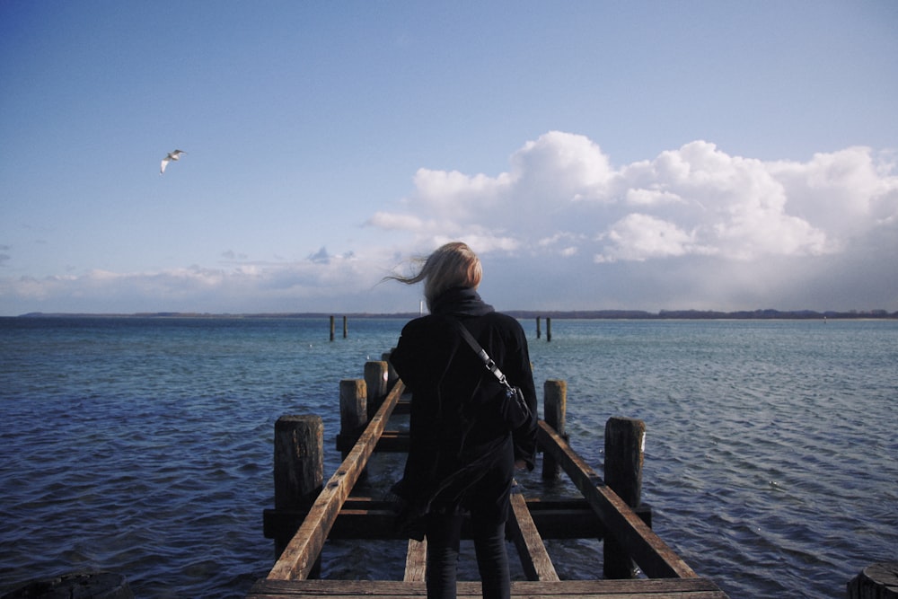 woman in black jacket standing on wooden dock during daytime