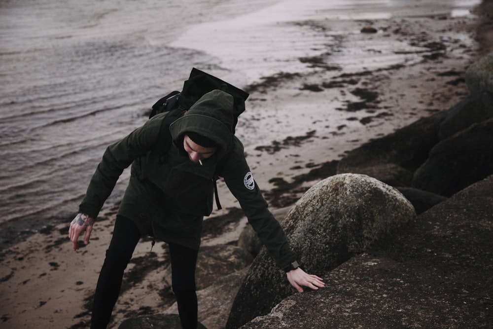 man in black jacket and black pants standing on rock near sea during daytime