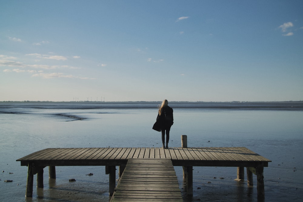woman in black long sleeve dress standing on brown wooden dock during daytime