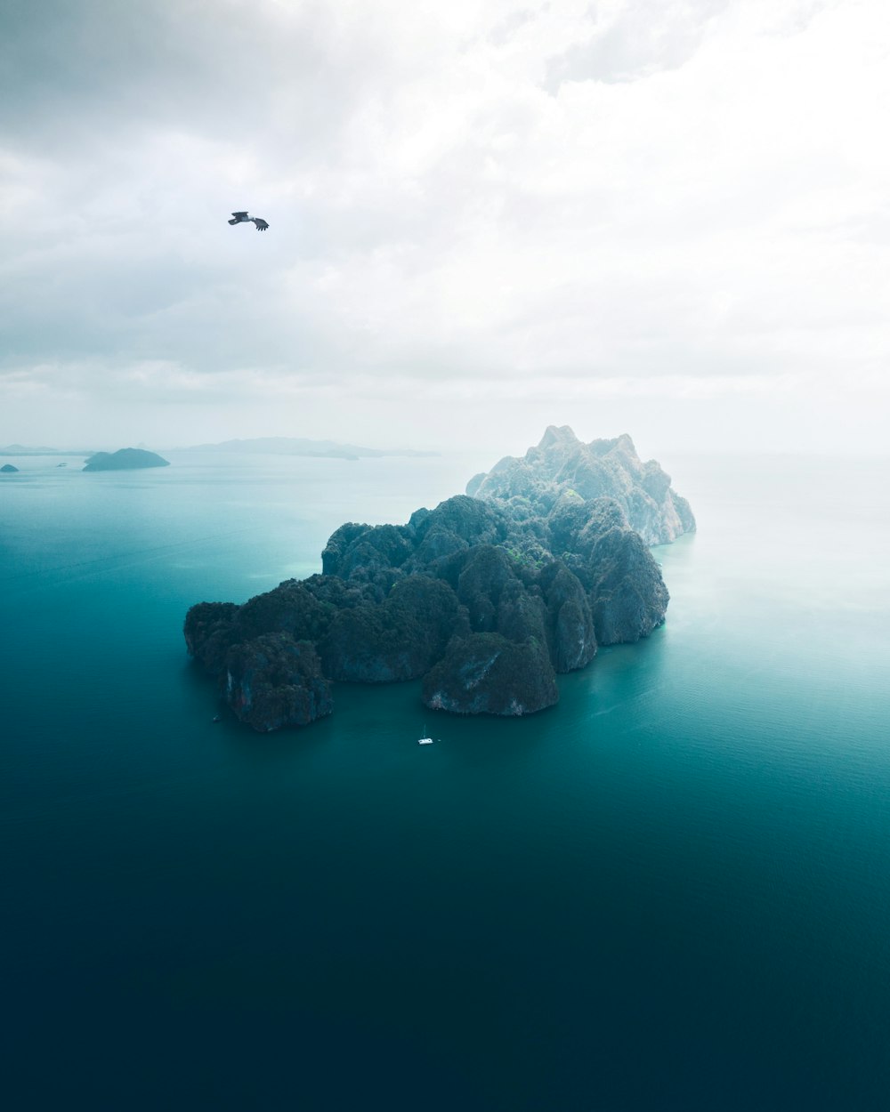 formação rochosa cinzenta no mar azul sob nuvens brancas durante o dia