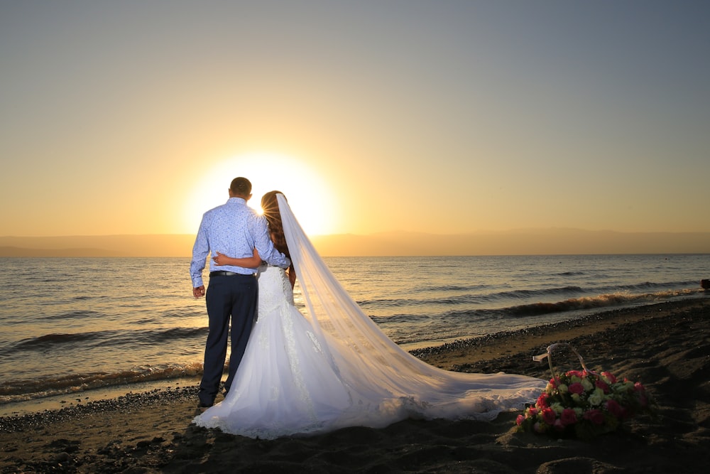 Mujer en vestido de novia blanco de pie en la playa durante la puesta del sol