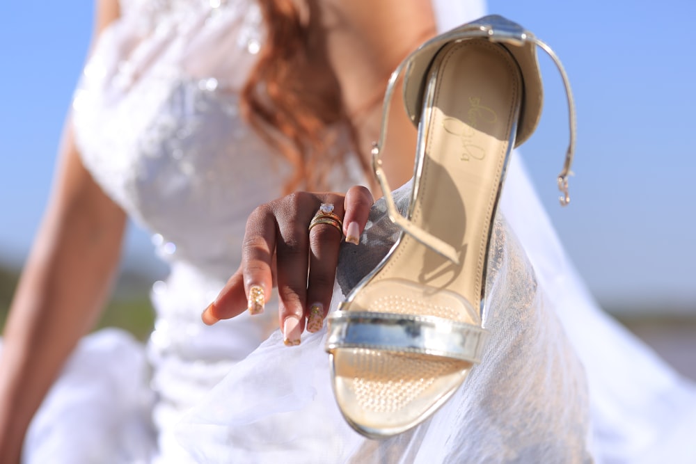 woman in white dress holding gold and white peep toe sandals