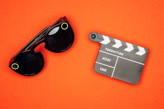 An orange background with black sunglasses featuring yellow accents and a black and white film clapperboard.