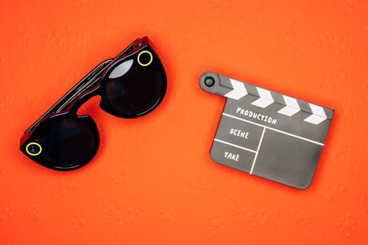 An orange background with black sunglasses featuring yellow accents and a black and white film clapperboard.