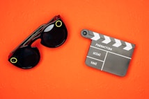 An orange background with black sunglasses featuring yellow accents and a black and white film clapperboard.