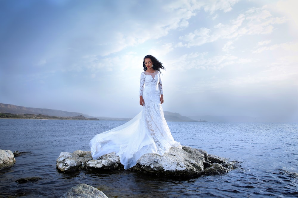Frau in weißem Kleid, die tagsüber auf einem Felsen in der Nähe des Meeres steht