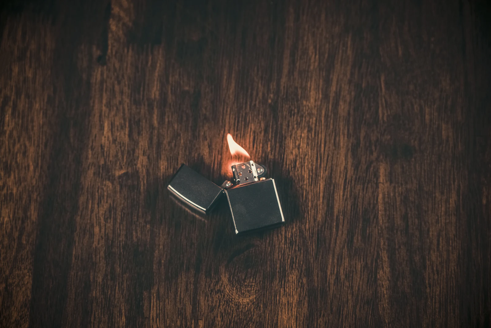 Open black metal windproof lighter burning on a dark wooden surface