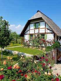 brown wooden house surrounded by green trees and flowers under blue sky during daytime