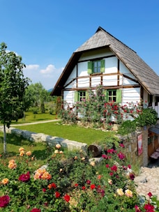 brown wooden house surrounded by green trees and flowers under blue sky during daytime