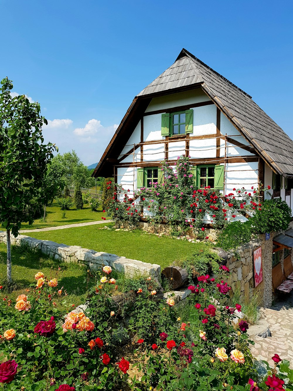 Maison en bois marron entourée d’arbres verts et de fleurs sous le ciel bleu pendant la journée