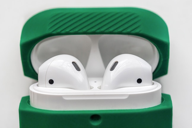 A pair of wireless earbuds resting inside an open charging case with a green cover. The earbuds are white, featuring a sleek and modern design, and the green cover adds a vibrant contrast.