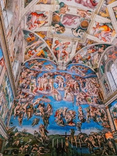 A detailed fresco covers the ceiling and wall of a large room, depicting numerous human figures in various poses, illustrating religious scenes. The artwork features vibrant colors and intricate details, illustrating a vivid narrative across the entire space.
