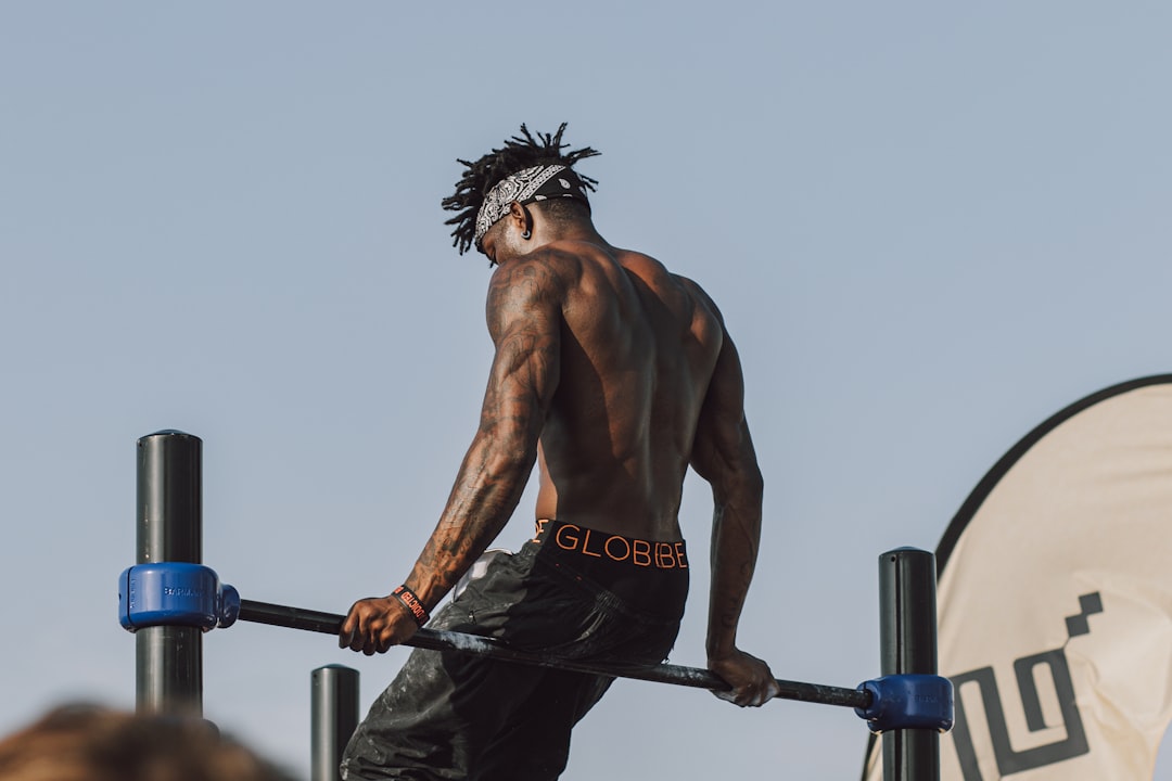 topless man in black shorts holding black exercise equipment