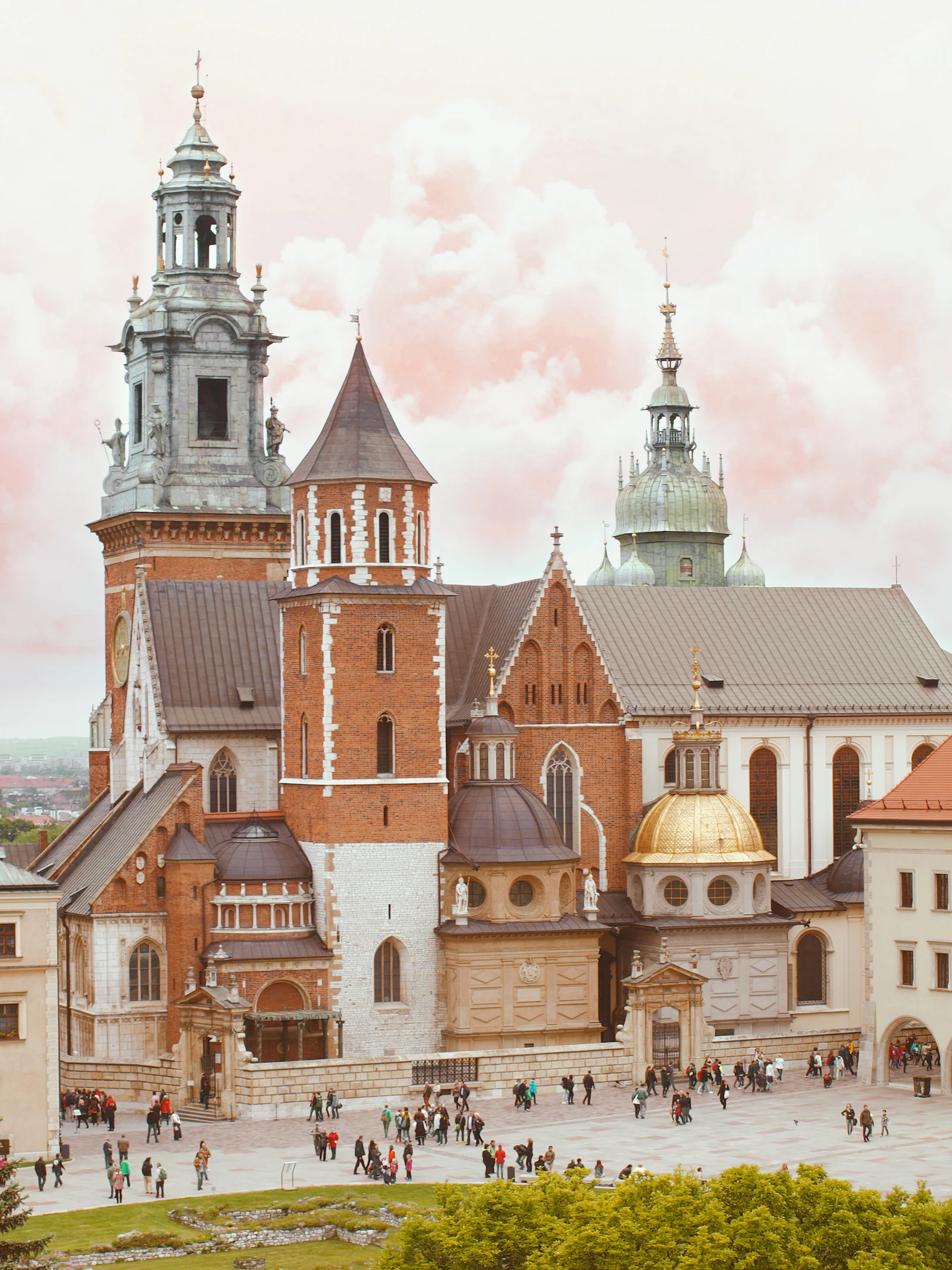 Wawel Cathedral in Krakow with its clock tower, brick chapels and gilded dome, seen from above the castle courtyard approach