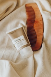 A wooden comb and a skincare product tube from The Ordinary are placed on a soft, cream-colored fabric. The items are carefully arranged, providing a cozy and natural aesthetic.