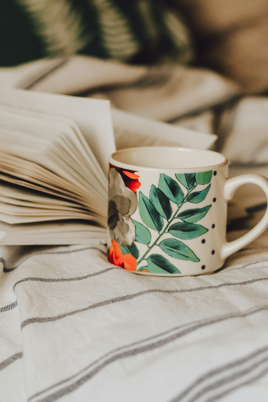 white green and red floral ceramic mug on white textile