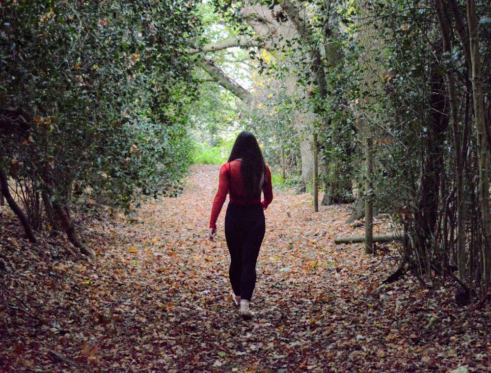 woman in red long sleeve shirt and black pants walking on forest during daytime