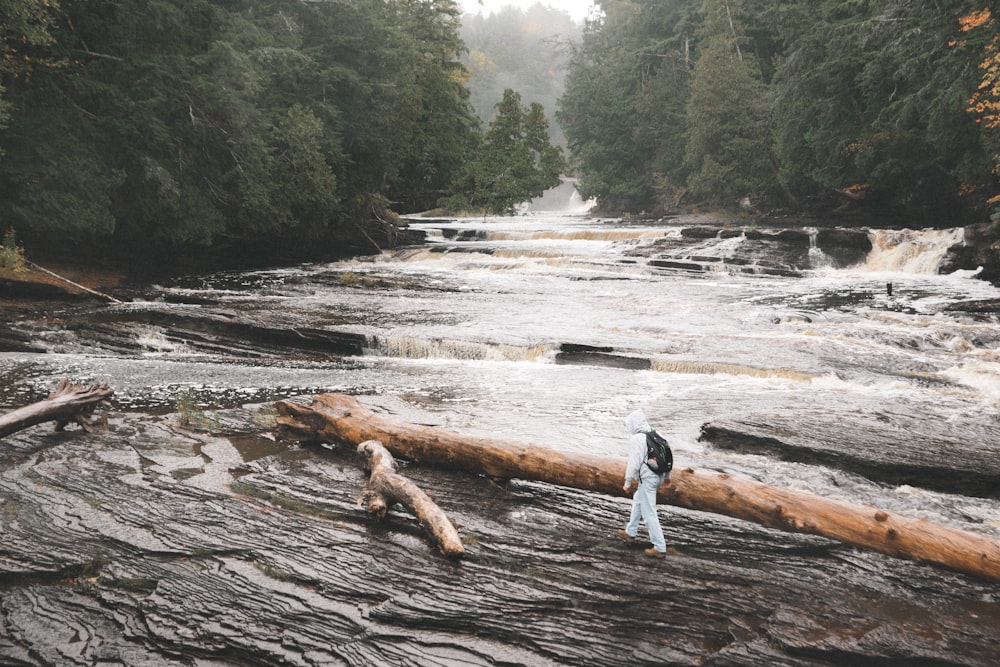 man in blue denim jeans standing on brown tree log on river during daytime