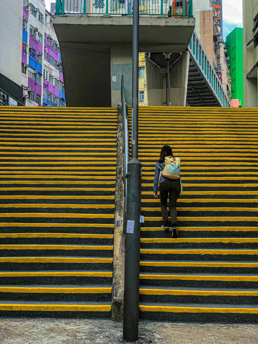 Mujer con camisa blanca y pantalones negros caminando por una escalera amarilla y gris