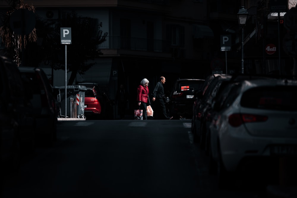 man in red jacket standing beside black car during night time