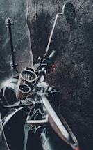 A close-up of a biker's hand gripping a motorcycle handlebar with a dark, industrial workshop background.