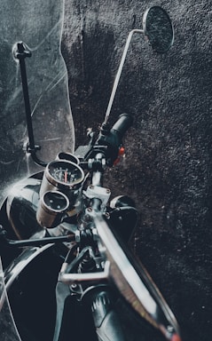 A close-up of a biker's hand gripping a motorcycle handlebar with a dark, industrial workshop background.