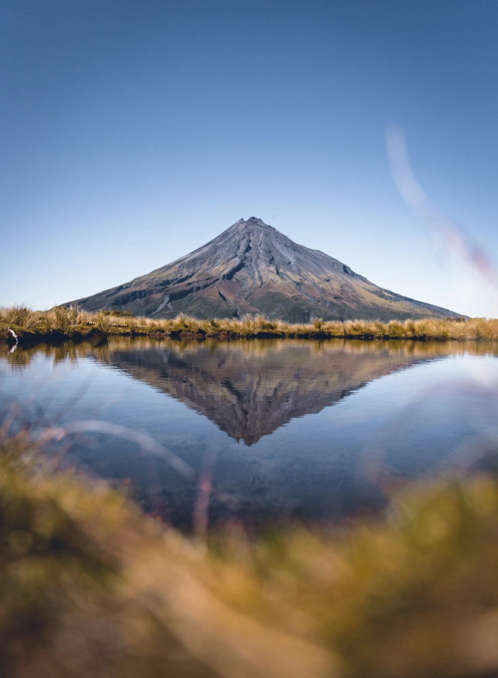 green and brown mountain beside lake under blue sky during daytime