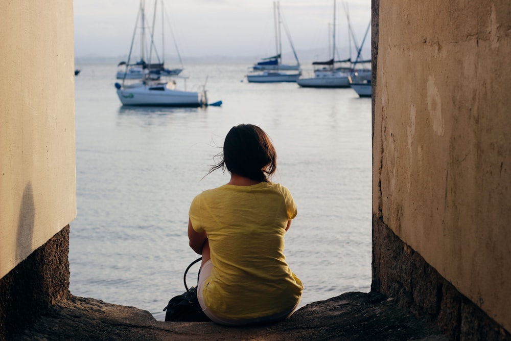 woman in yellow shirt sitting on brown wooden log near body of water during daytime