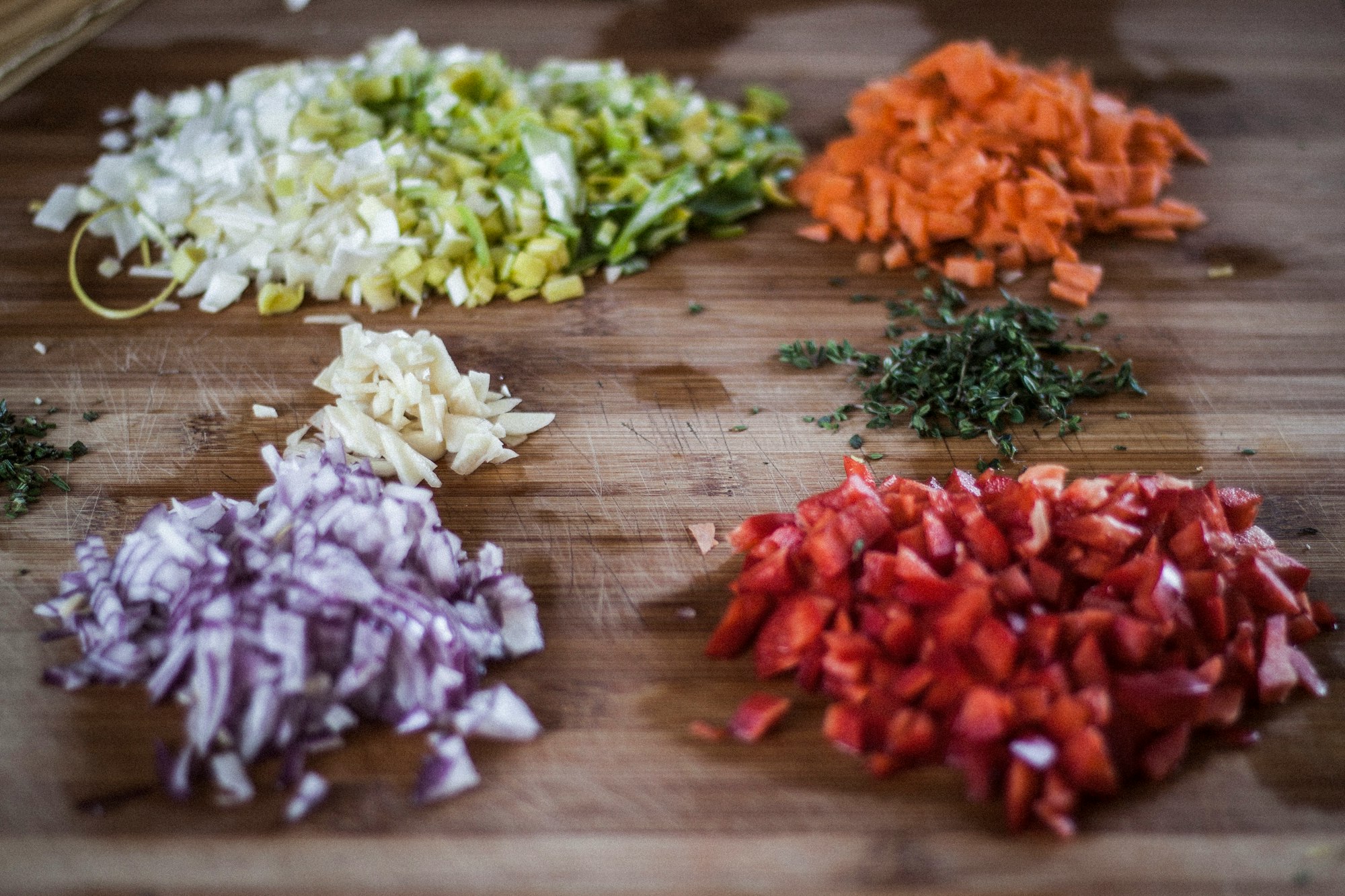 A chopping board with diced vegetables and herbs