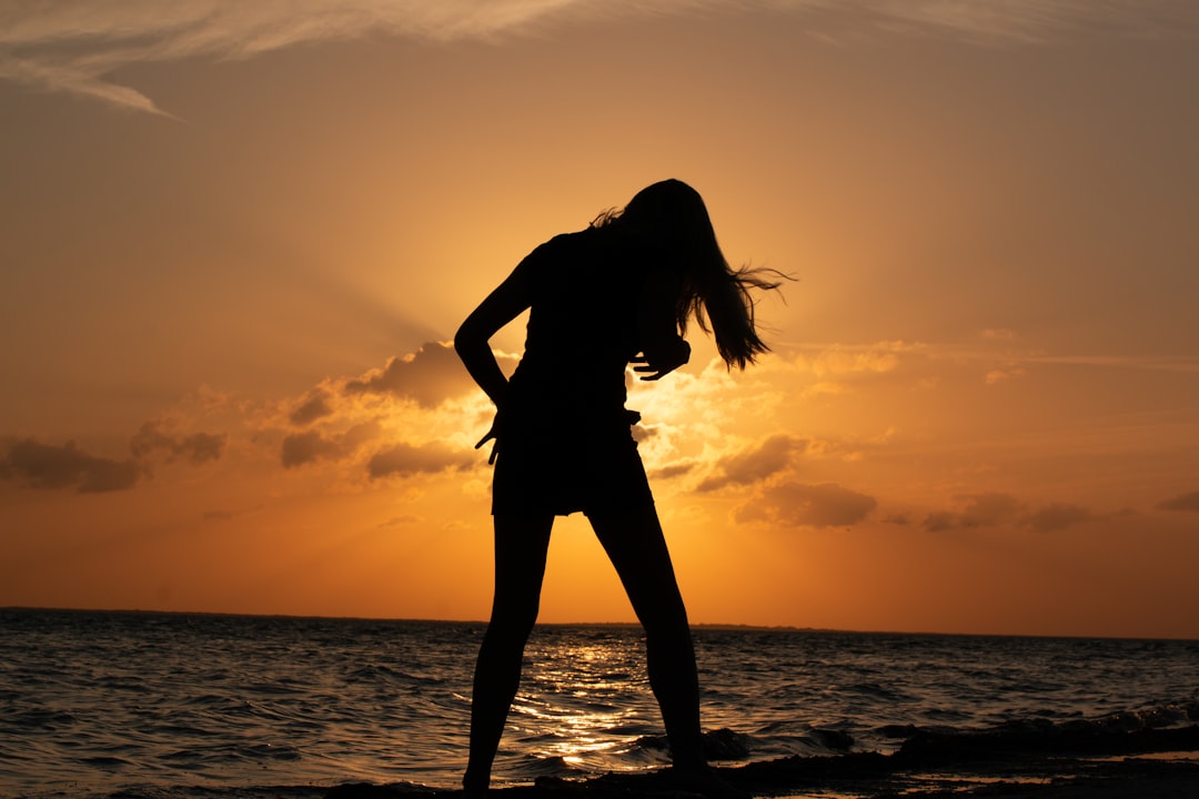 silhouette of woman standing on beach during sunset