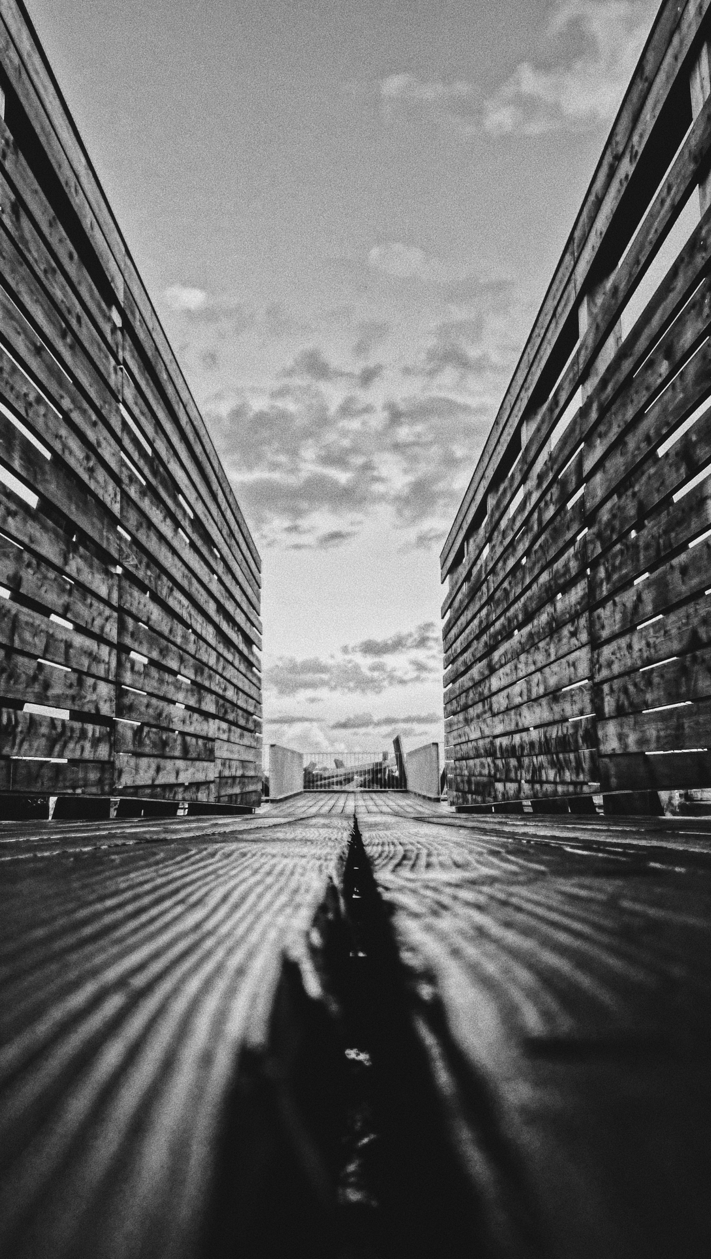 grayscale photo of person walking on pathway between concrete buildings
